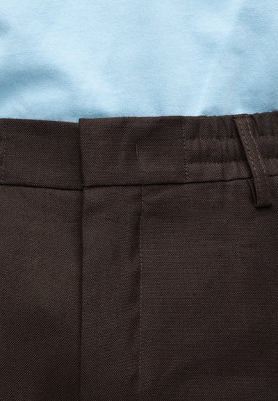 Gros plan sur la taille d'un pantalon marron avec passants de ceinture et chemise bleu clair rentrée à l'intérieur.