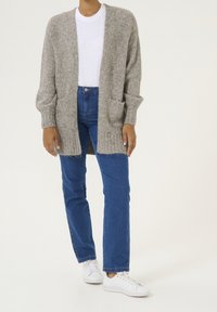 Graue, strukturierte Strickjacke mit offenem Vorderteil, gerippten Bündchen und zwei Taschen, kombiniert mit blauen Jeans und weißen Sneakern.