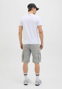 Weißes T-Shirt mit kurzen Ärmeln, graue Cargo-Shorts mit Seitentaschen, weiße Socken mit schwarzen Streifen und graue Sportschuhe, von hinten betrachtet.