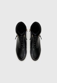Bottines en cuir noir avec une texture lisse, dotées de finitions dorées, d'un système de laçage à l'avant et de fermetures éclair sur les côtés pour un enfiler facile.