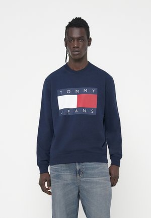 Felpa blu navy con scollatura a girocollo, caratterizzata da una grafica rettangolare bianca e rossa e testo "TOMMY JEANS" sulla parte anteriore.