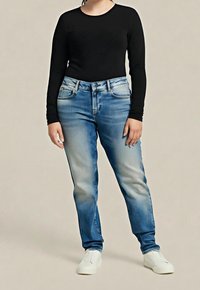 Černý top s dlouhým rukávem, džíny s přechodem z světle modré do tmavě modré, rovný střih nohavic a bílé nazouvací boty. Hladký materiál s jemnými texturálními detaily.