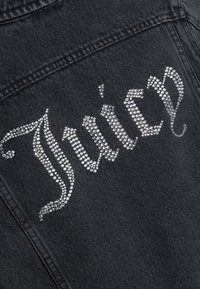 Μαύρο τζιν ύφασμα με τη λέξη "Juicy" γραμμένη με ασημένιες στρας σε διακοσμητικό στυλ γραφής.