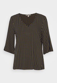 Svart topp med gula prickar, V-ringning och trekvartsärmar; tillverkad i ett slätt tyg med en lös, flödande design.