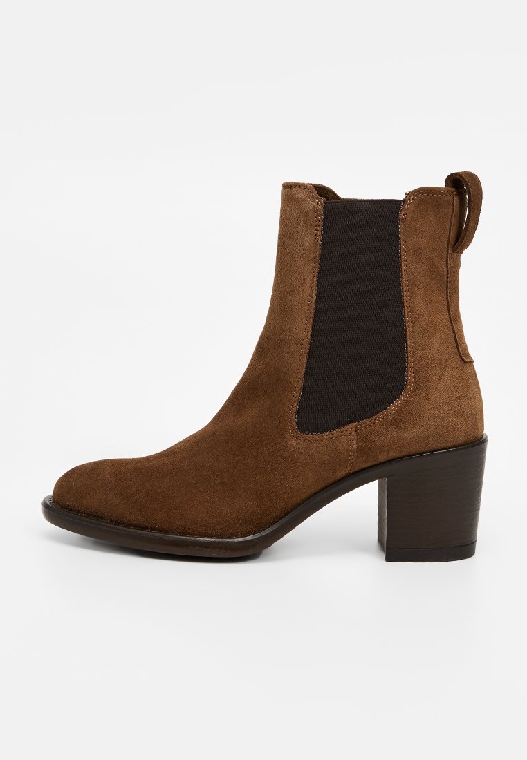 Bottine en suédine marron avec un bout rond, des panneaux latéraux élastiques et un talon large et stable. Texture lisse avec un design minimaliste.
