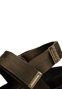 Brown textile sandals featuring crisscross straps, gold-tone hardware accents, and a textured sole for grip.