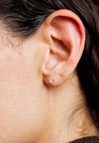Cercel mic din argint, în formă de floare, cu trei accente de diamant, purtat pe lobul unei urechi umane. Textura pielii vizibilă.