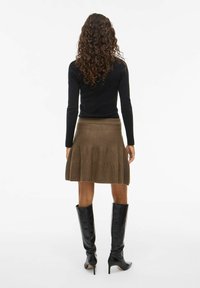 Jupe évasée marron, arrivant aux genoux, avec une taille côtelée, associée à un haut noir ajusté à manches longues et des bottes noires à talons hauts.