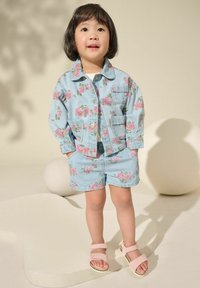 Denim-takki ja shortsit setti, jossa on vaaleanpunaisia ja vihreitä kukkakuvioita, lyhyet hihat ja kaksi etutaskua. Vaaleanpunaiset sandaalit säädettävillä hihnoilla.