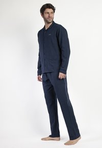 Conjunto de pijama a rayas azul marino hecho de un tejido suave, que incluye una camiseta abotonada con dos bolsillos y pantalones rectos a juego.