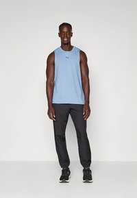 Hele sinine lõhkise mustriga varrukateta sportlik särk, mida on kombineeritud mustade kitsenevate pükste ja mustade tossudega.