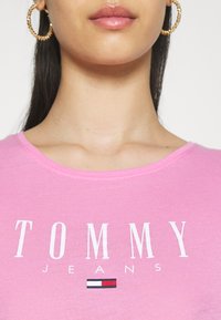 Różowy bawełnowy t-shirt z okrągłym dekoltem i wyraźnym białym napisem "TOMMY JEANS" z małym logo w kolorach czerwonym, białym i niebieskim poniżej.