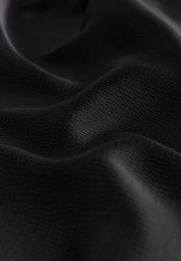 Close-up view of black textured fabric with smooth, curved folds and subtle light reflections.