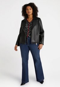 Jachetă din faux leather neagră, cu un fermoar asimetric și guler cu colți, purtată cu o bluză cu buline și blugi evazați albaștri.