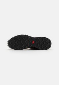 Sola de sapatilha de trail running com uma superfície de borracha preta texturizada, com cravos multidireccionais e um destaque vermelho no centro para tração.