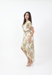Blommönstrad klänning i vitt, med korta volangärmar och en asymmetrisk nederkant. Kombinerad med transparenta blockklack-sandaler.