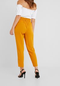 Yellow, tapered pants with a high, elastic waistband; paired with a white off-shoulder top. Black high-heeled sandals are worn.