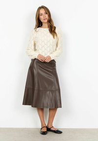 Krémový pletený top s dlhými rukávmi a vlnkovým vzorom, kombinovaný s tmavo hnedou koženou midi sukňou. Čierne topánky dotvárajú outfit.
