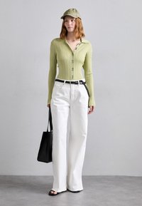 Camicetta a maniche lunghe a righe verde chiaro, pantaloni bianchi a gamba larga, cintura nera, borsa a tracolla nera e cappello verde oliva. Texture morbide visibili.