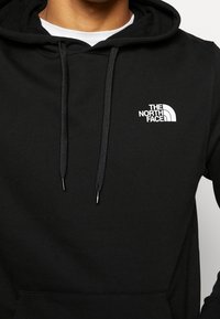 Czarna bluza z kapturem wykonana z miękkiego materiału, posiadająca przednią kieszeń kangurkę, regulowany kaptur ze ściągaczem oraz białe logo na lewej piersi.