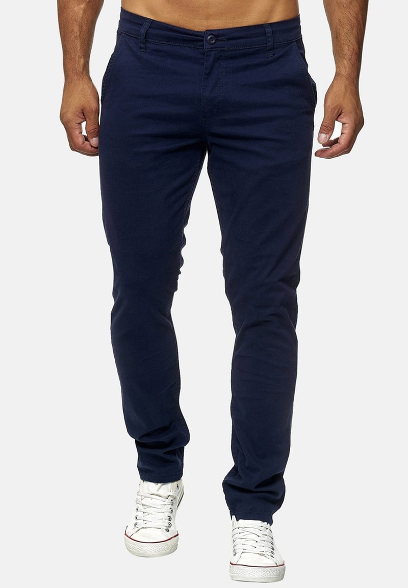 Pantalones de algodón azul marino con un ajuste entallado, que cuentan con bolsillos delanteros y cremallera. Combinados con zapatillas blancas. Textura suave, diseño casual.