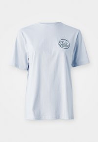 T-shirt di cotone azzurro chiaro con maniche corte, che presenta un logo grafico circolare blu scuro nella zona sinistra del petto.