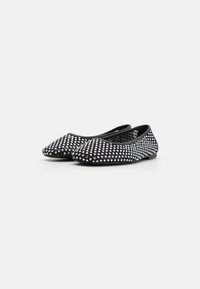 Pantofi negri, cu talpă plată, vârful ascuțit și toc mic, având un model de cuie argintii pe întreaga suprafață superioară. Material flexibil, cu un finisaj neted.