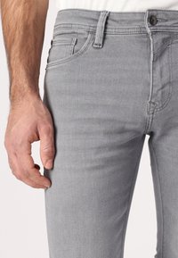 Sive traperice slim kroja, s ravnim prednjim dijelom, standardnim džepovima i kopčanjem na dugme. Glatka tekstura i minimalni detalji šivanja.