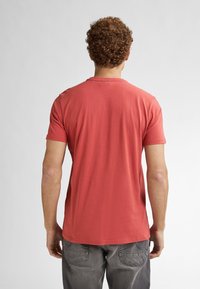 T-shirt in cotone rosso con maniche corte, collo rotondo e vestibilità rilassata. La vista posteriore mostra una texture liscia e un design semplice.