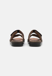 Braune Ledersandalen mit offenem Fersenbereich, ausgestattet mit zwei verstellbaren Riemen, einem gepolsterten Fußbett und einer schwarzen Gummisohle.