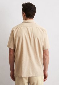 Korte mouwen overhemd in lichtbeige gestructureerde stof met een rechte zoom. Beschikt over een puntig kraag en naaddetails op de rug.