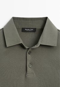 Olivgrünes Polohemd mit gerippter Textur, zwei Knöpfen und einem strukturierten Kragen. Das Etikett trägt die Aufschrift "Massimo Dutti", hergestellt in Marokko.