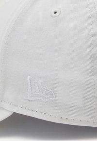 Boné de beisebol branco feito de tecido com uma superfície texturizada. Apresenta um logótipo bordado de um lado e ilhoses de ventilação.