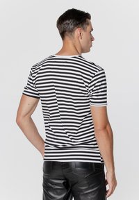 Czarno-biały pasiasty t-shirt z krótkim rękawem i okrągłym dekoltem, charakteryzujący się dopasowanym krojem i gładką fakturą materiału. Noszony z czarnymi skórzanymi spodniami.