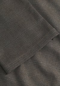 Tessuto marrone con texture e un sottile motivo a quadretti, caratterizzato da una superficie liscia e cuciture a contrasto lungo i bordi.