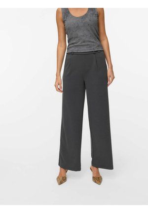 Pantalons larges en gris foncé, en tissu lisse, avec des plis à l'avant et une simple taille élastique. Débardeur texturé gris au-dessus.