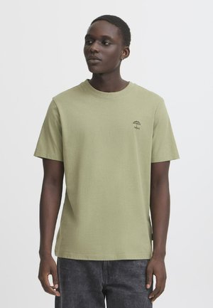 Kortærmet grøn linned t-shirt med rund halsudskæring, prydet med et lille sort paraplylogo på brystet, parret med mørkegrå jeans.