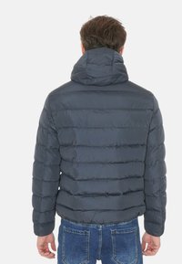 Giacca a vento grigia con design a righe verticali, cappuccio e texture leggermente lucida. Indossata con jeans in denim blu.