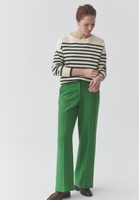 Pruhovaný svetr v krémové a tmavě zelené barvě, spárovaný s vysokými zelenými kalhotami. Slim fit, hladká textura, s minimalistickým designem.