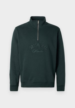 Dark green sweatshirt with a high collar and a half-zip closure. Features embossed "ORIGINALS Studio" text on the front. Soft texture.