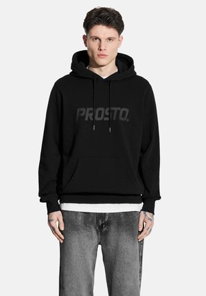 Czarna bluza z kapturem, wykonana z mieszanki bawełny, z przestronną kieszenią kangurzą i dużym, matowym logo "PROSTO." Nosisz ją na białej koszulce.