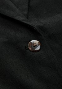 Black fabric with a textured surface featuring a round, brown and cream marbled button with four holes, stitched into the material.
