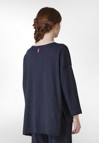 Marineblauer, oversized Pullover mit rundem Halsausschnitt, drei Viertelärmeln und einem rosa Etikett auf der Rückseite; aus weichem, strukturiertem Stoff gefertigt.