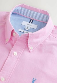 Camisa rosa de corte ajustado con botones, con rayas en el cuello interior de color azul claro y un pequeño logotipo de ciervo bordado en azul.