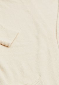 Cardigan lavorato a maglia in bianco sporco, con una texture morbida, dotato di maniche lunghe e tasche a toppa, con un design semplice e casual.