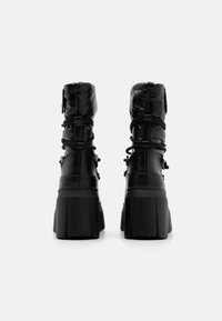 Botas de plataforma negras con un acabado brillante, que presentan un upper acolchado, un diseño fruncido y una suela de goma gruesa. Cierre con cordones detallado y ajustes de toggle.