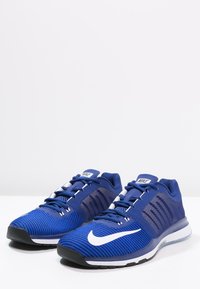 Modré sportovní boty s pletenou texturou, s bílým logem Nike, černou podrážkou a síťovinovými panely pro prodyšnost.