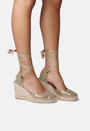 Gold espadrille wedges with a textured woven upper and ribbon ankle ties, featuring a natural jute rope sole. Smooth, shiny finish.