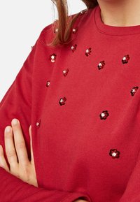 Roter Baumwoll-Sweatshirt mit floralen Paillettenverzierungen in Rot und Schwarz. Runder Kragen und lange Ärmel, mit einer glatten Textur.