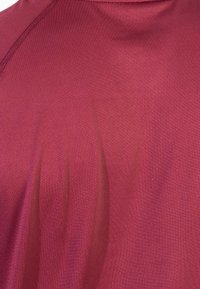 Bordowa sportowa koszulka wykonana z gładkiego, elastycznego materiału. Posiada okrągły dekolt i subtelny wzór z delikatnymi zagnieceniami.